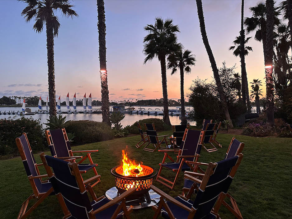 Rocking chairs surrounding bonfire with marina in background at sunset