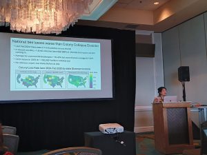 An individual at a podium next to a large screen with a projected presentation.