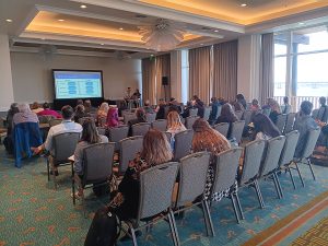 Two individuals at a podium with a presentation projected onto a screen.
