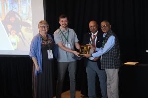 Photo of the individual holding an award with three colleagues standing next to the individual.