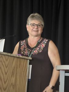 A photo of a woman in a black dress standing behind a podium.