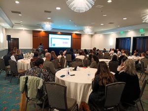 Attendees in a meeting room seated at round tables.