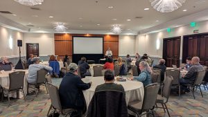 Image of people seated a round tables listening to a speaker.